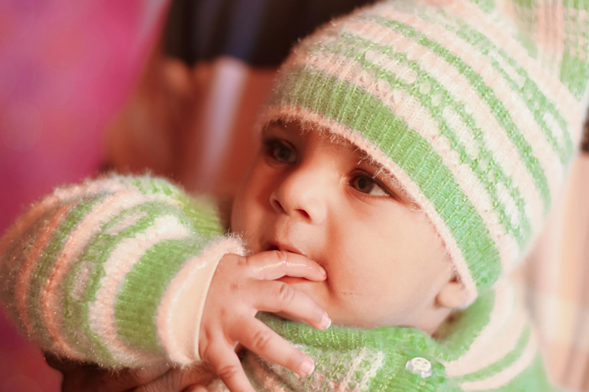 Niemowlę w zielonej czapce i swetrze z wełny merino ssie palce