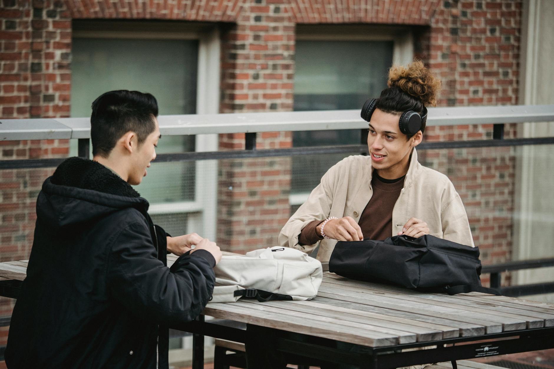 Dwóch młodych mężczyzn przy stoliku na zewnątrz w codziennych stylizacjach