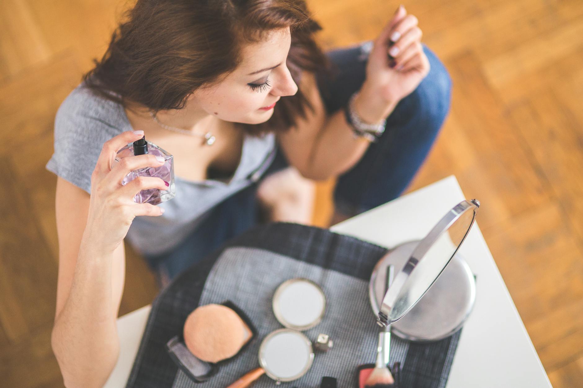 Młoda kobieta spryskuje się perfumami przy kosmetykach do makijażu