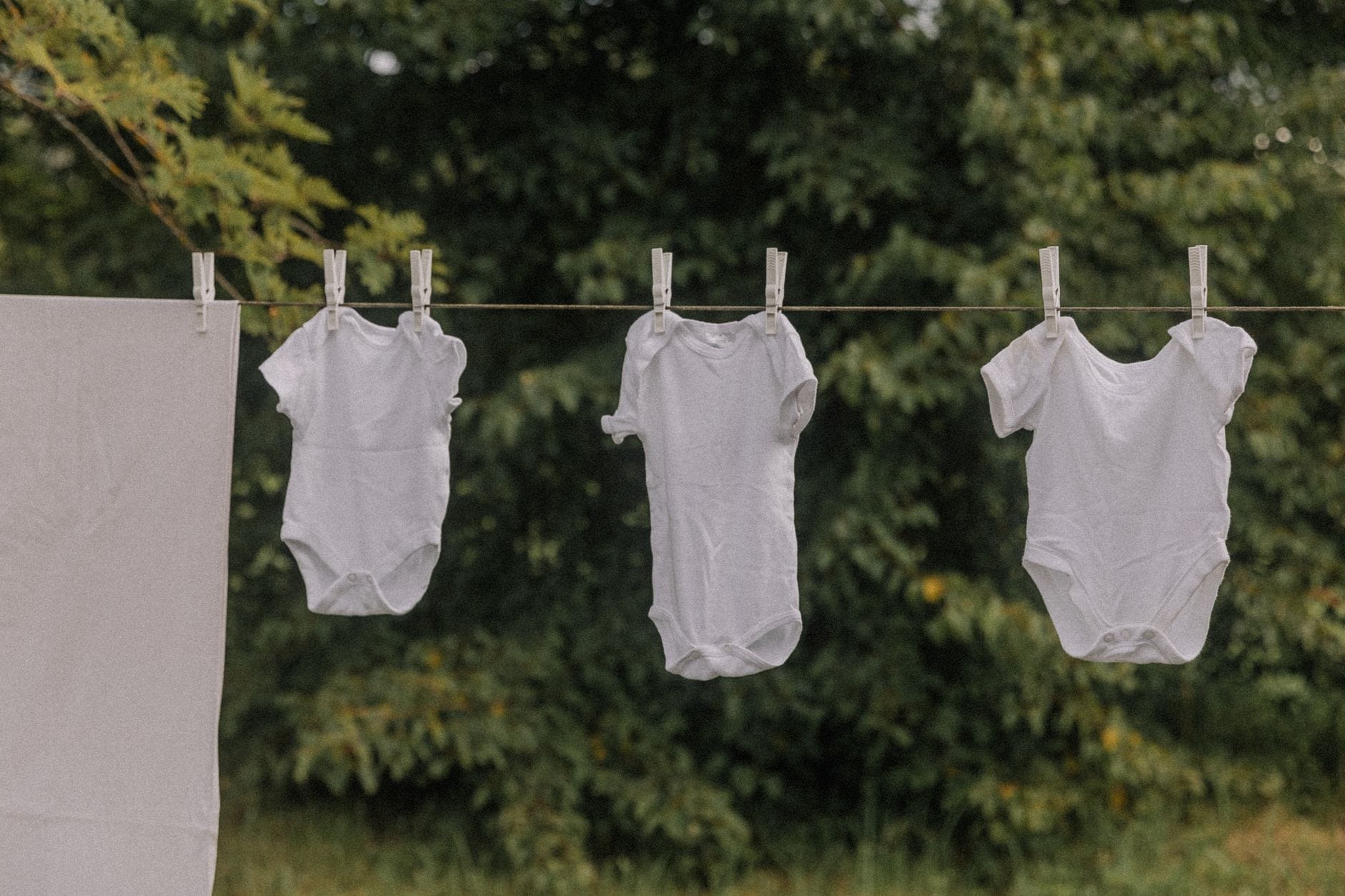 Białe body niemowlęce z bawełny suszące się na sznurku na dworze