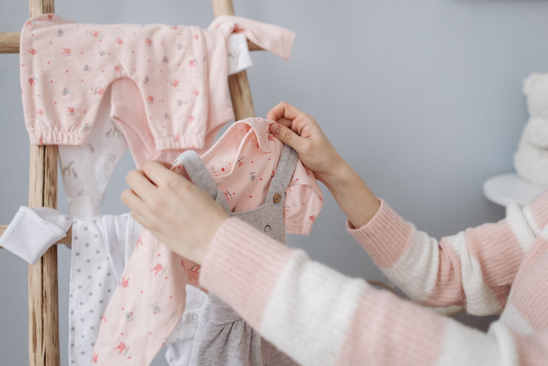 Mama wiesza kolorowe ubranka niemowlęce na drewnianym stojaku