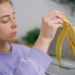 Kobieta wrzuca obierkę banana do kosza na odpady kuchenne