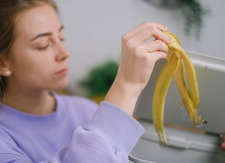 Co można wrzucać do kompostownika kuchennego, a czego lepiej unikać? Kobieta wrzuca obierkę banana do kosza na odpady kuchenne