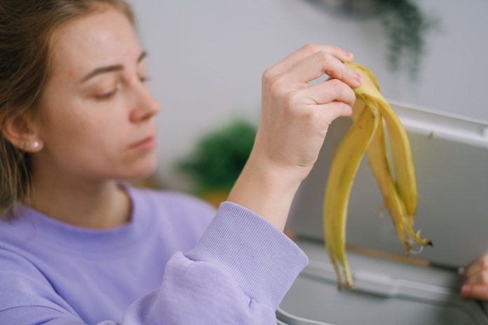 Kobieta wrzuca obierkę banana do kosza na odpady kuchenne Kobieta wrzuca obierkę banana do kosza na odpady kuchenne